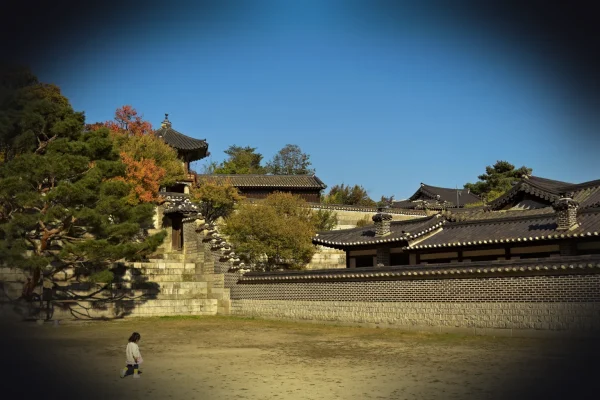 Child walks across grassy field near traditional korean buildings.