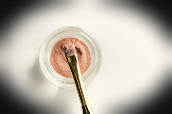 brown makeup brush in front pink powder on glass case