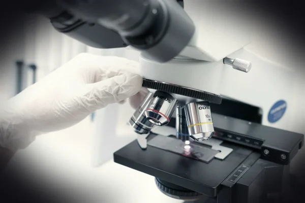A person in white gloves looking through a microscope