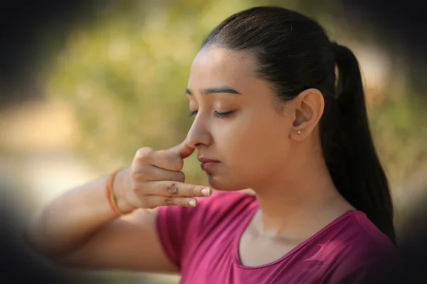A young woman practicing alternate nostril breathing outdoors.