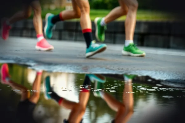 Runners' legs reflected in a puddle on the road.