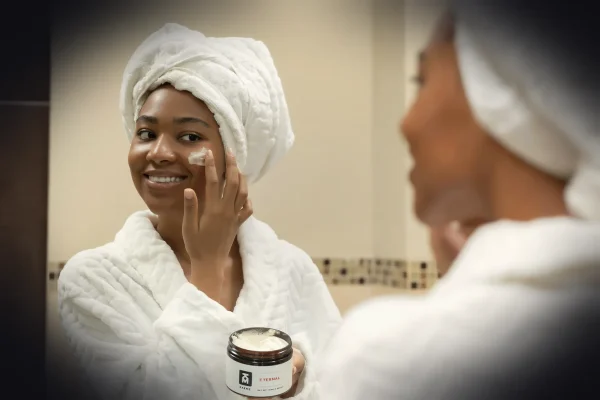 a woman with a towel on her head and a jar of cream on her face