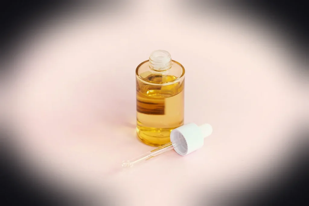 Skincare serum bottle and dropper on a pink surface.