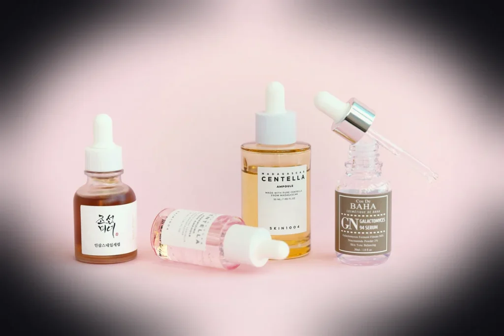 Skincare serums and dropper bottles sit on pink.