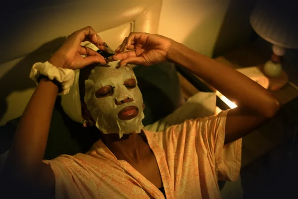 A woman applies a sheet mask in bed.